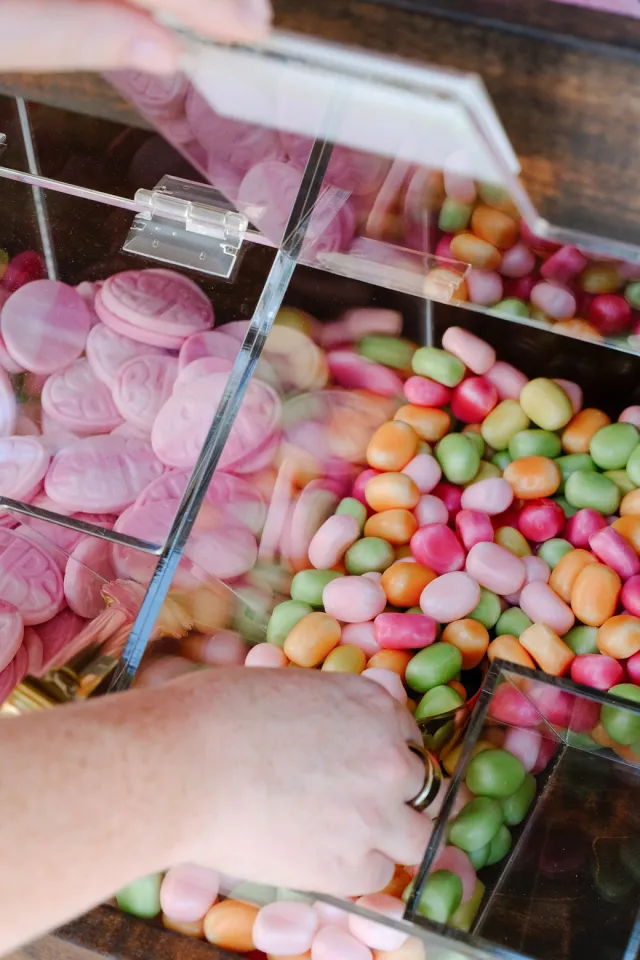 A hand scoops colorful Swedish candy from a clear bin beside pink BUBS