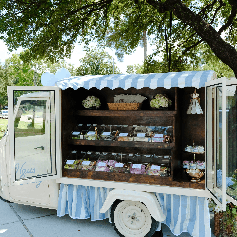 Haus Candy Cart with a blue-and-white awning beneath a tree
