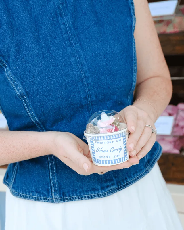 A guest in a denim top holding a lidded Haus Candy cup filled with mixed candy