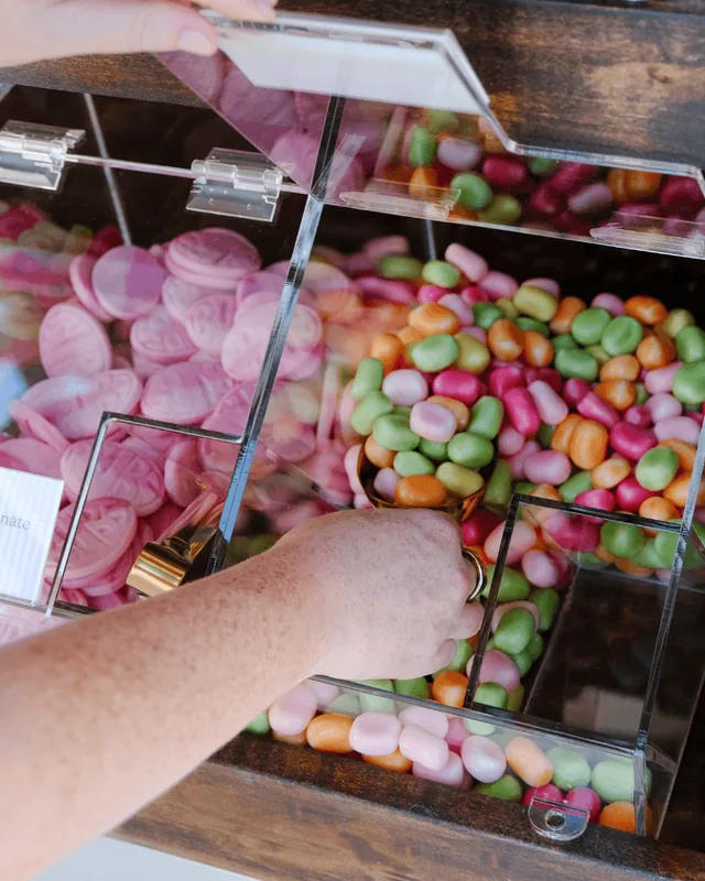 A hand scooping colorful candy-coated chews from a clear bin beside pink BUBS