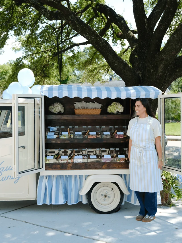 An attendant in a striped apron stands beside the fully stocked Haus Candy Cart