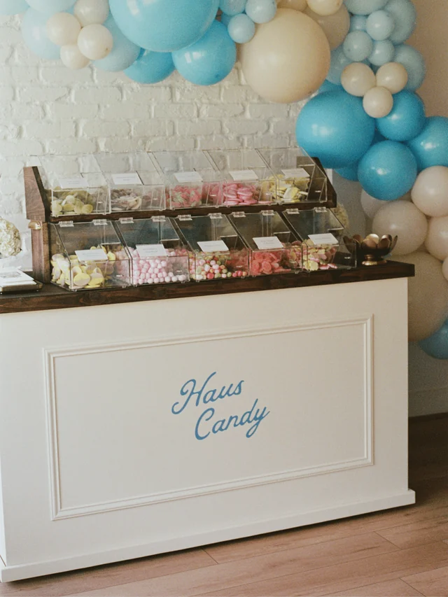 White Haus Candy Stand with clear candy bins beneath a blue-and-cream balloon garland