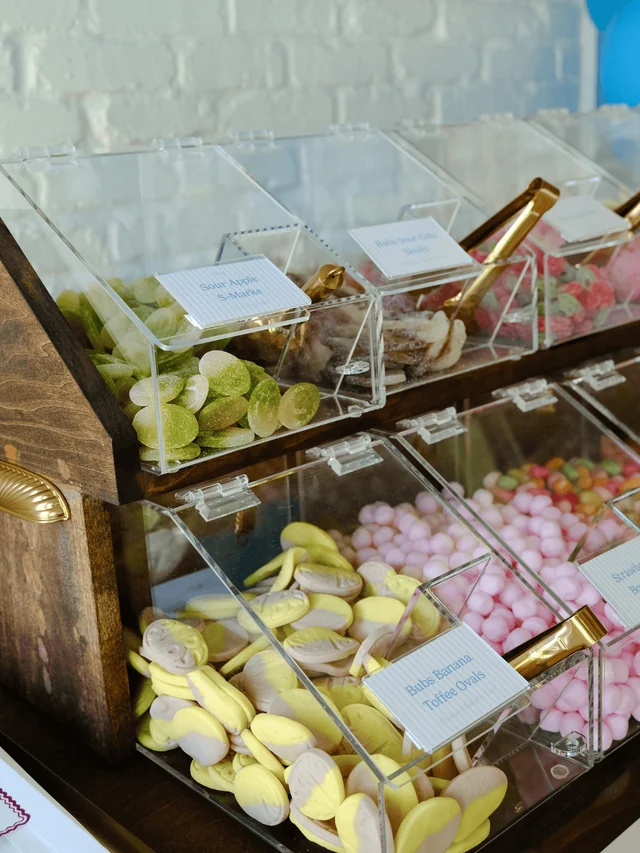 Close-up of labeled sour apple gummies and banana toffee ovals in clear candy bins