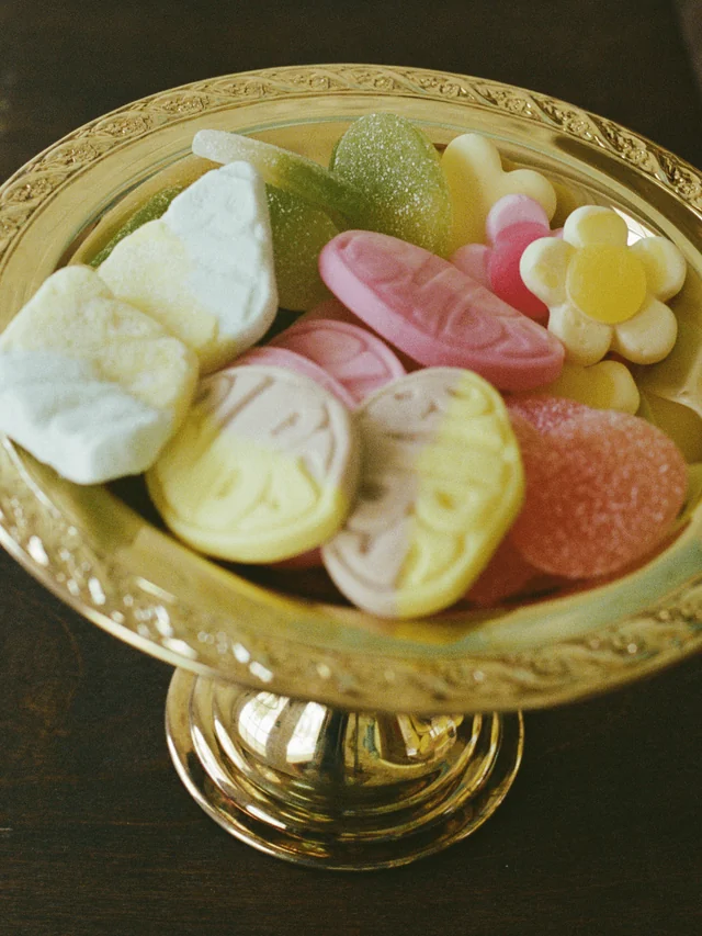 Pastel foam candies, sugar-coated gummies, and a flower-shaped sweet on a gold pedestal dish
