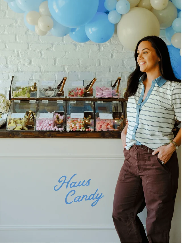 A guest stands beside the indoor Candy Stand under blue and cream balloons