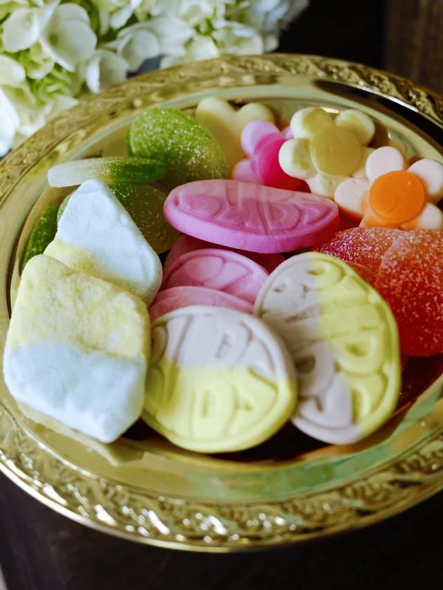 A gold platter holds pink and yellow foam ovals, sour gummies, and flower-shaped candy