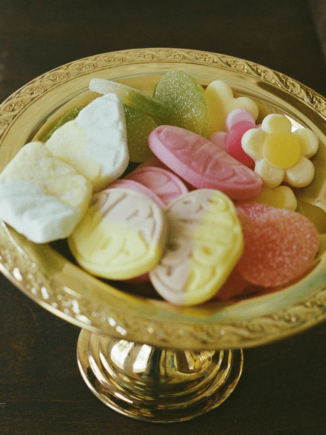 A gold footed bowl displays a mix of pastel foam sweets and sugar-coated gummies